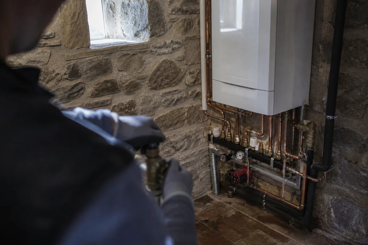 Chaufferie de maison ancienne avec chaudière murale à condensation et raccordements en cuivre