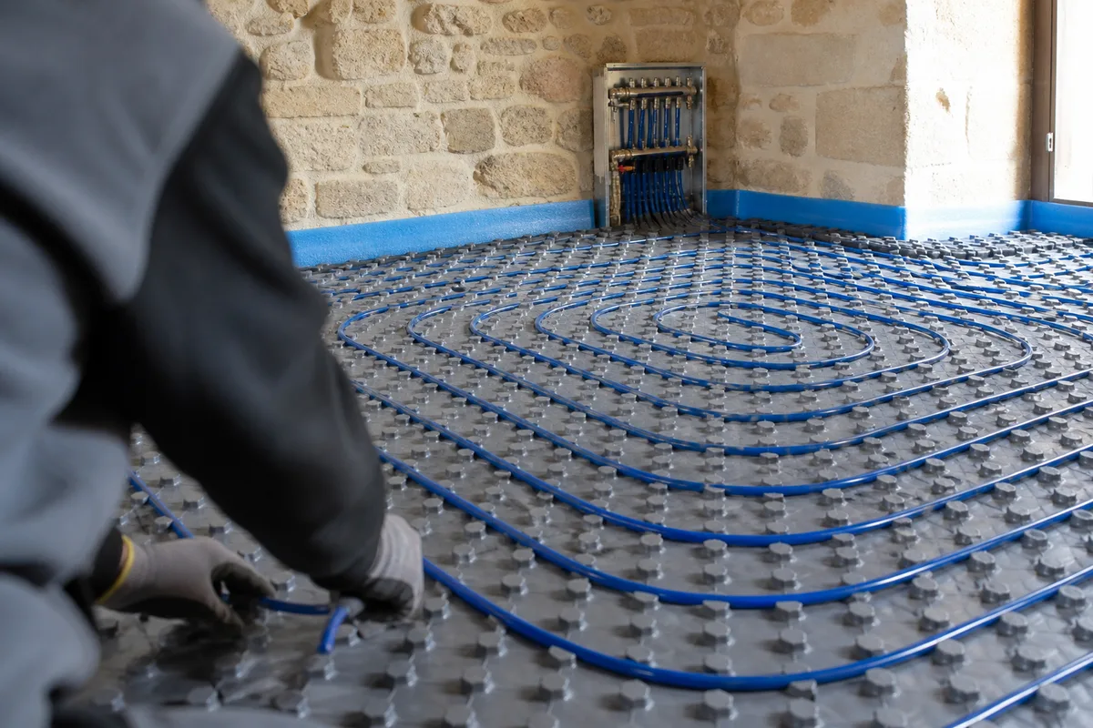 Boucles de plancher chauffant posées sur isolant dans une pièce aux murs de pierre