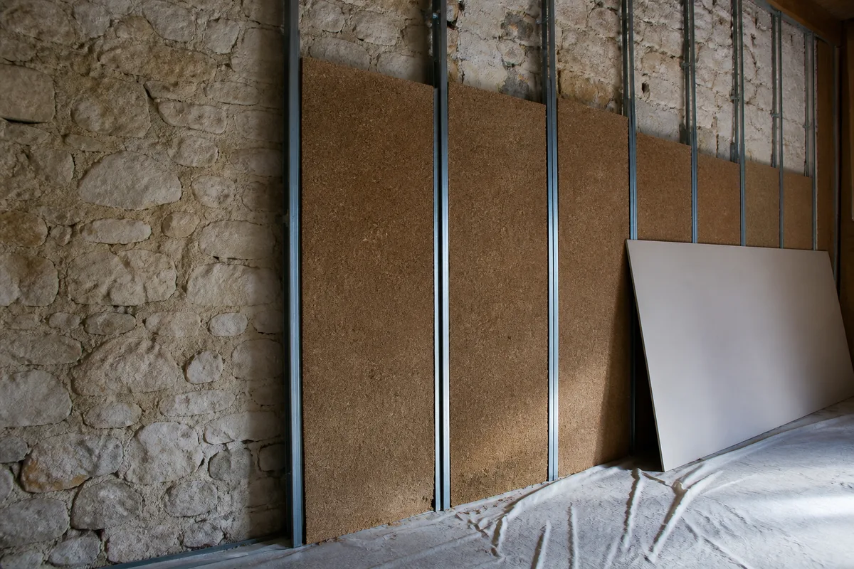 Contre-cloison en cours de montage sur ossature devant un mur de moellons calcaires